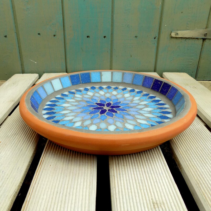 A mosaic bird bath with a mandala style design made with shades of blues and turquoise tiles